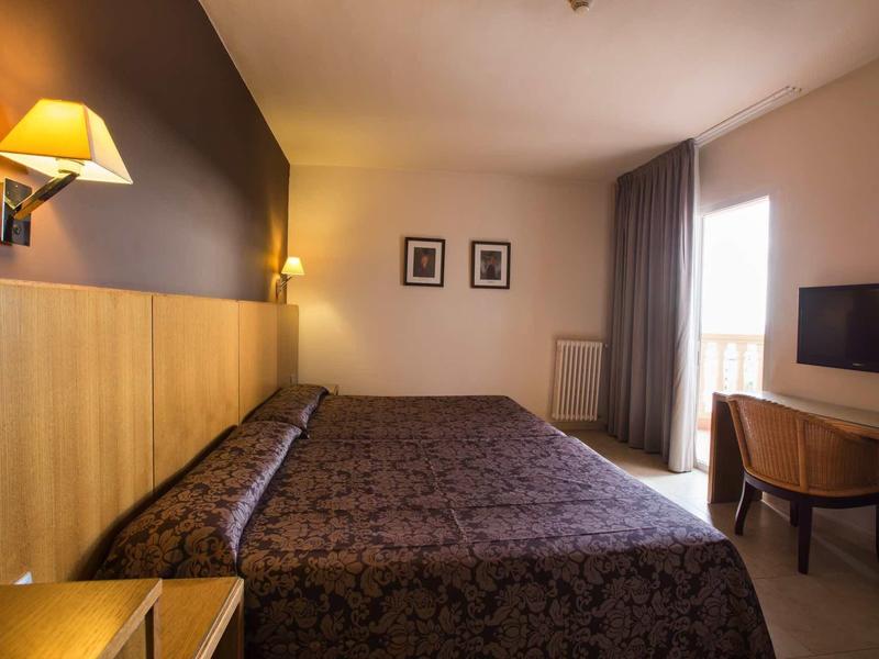 Cozy hotel room with double bed, wall lamps, curtains, and a desk with a TV.