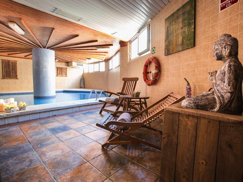 Indoor spa area with pool, wooden lounge chairs, and a Buddha statue on a cabinet.