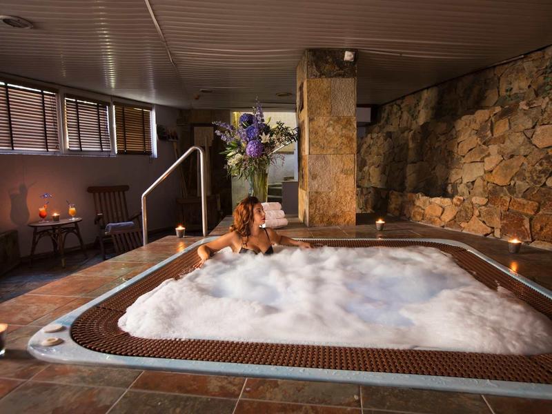 Cozy indoor hot tub room with stone walls, soft lighting, and a teddy bear by the tub.
