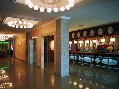 Hol hotelowy z błyszczącą podłogą, windami i dekoracyjnym oświetleniem sufitowym.