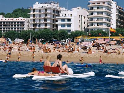Ludzie relaksują się na łodzi na wodzie z ruchliwą plażą i budynkami w tle.