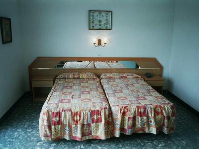 Pokój z dwoma pojedynczymi łóżkami, szafkami nocnymi i lampką na ścianie w prostym zakwaterowaniu