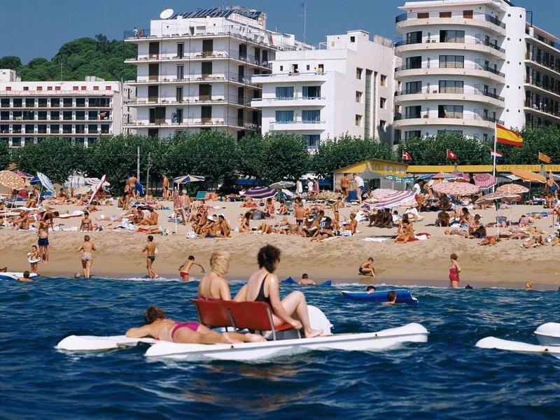 Ludzie relaksują się na łodzi na wodzie z ruchliwą plażą i budynkami w tle.