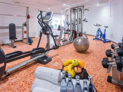 Salle de sport moderne avec appareils d'entraînement, haltères et serviettes dans une pièce lumineuse.