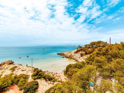 Küste mit Sandstrand, Felsen, türkisblauem Meer und bewachsenen Hügeln unter blauem Himmel.
