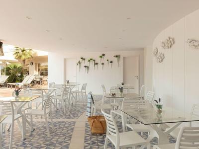 Moderner Außenbereich mit weißen Metallstühlen, Glastischen und Wandpflanzen in hellem Ambiente.