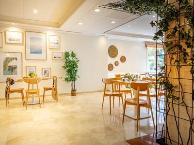 Heller, moderner Speisesaal mit Holztischen, Pflanzen und Wanddekoration.