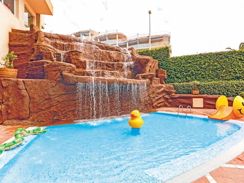 Hellblauer Pool mit gelben Gummienten und brauner Felsen-Wasserfallwand im Außenbereich.