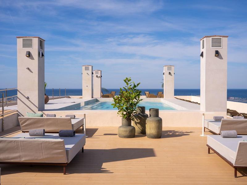 Dachterrasse mit Pool, Sitzbereichen und Meerblick bei klarem Himmel.