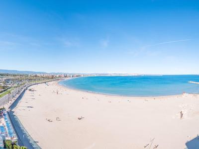 Rozległa piaszczysta plaża z czystym niebieskim niebem i spokojnym morzem w miejscu wakacyjnym.