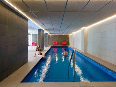 Hotelowy basen kryty z ludźmi pływającymi i siedzącymi obok.