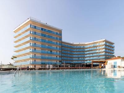 Nowoczesny budynek hotelu z dużymi szklanymi oknami obok basenu pod czystym niebem.