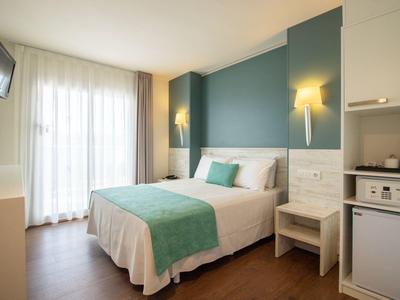 Jasny pokój hotelowy z łóżkiem dwuosobowym, zielono-niebieską ścianą i drewnianą podłogą.