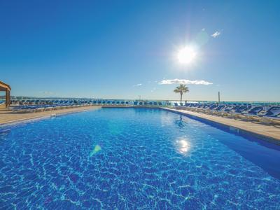 Przejrzysta niebieska woda w basenie na zewnątrz z niebieskimi leżakami i parasolami w słoneczny dzień.