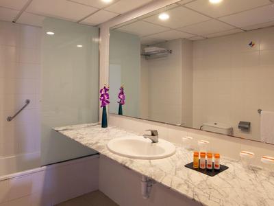 Jasna łazienka z marmurowym blatem, umywalką, dużym lustrem i wanną z przegrodą szklaną.