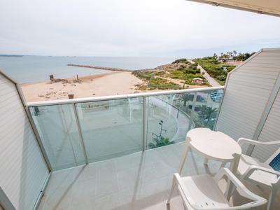 Balkon z szklanym balustradą, stołem i krzesłami z widokiem na plażę i morze.