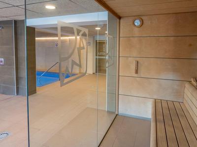 Nowoczesna sauna z drewnianą boazerią i panoramicznym oknem z widokiem na przyległy basen.