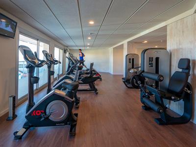 Nowoczesna siłownia z kilkoma maszynami do ćwiczeń i dużymi oknami.