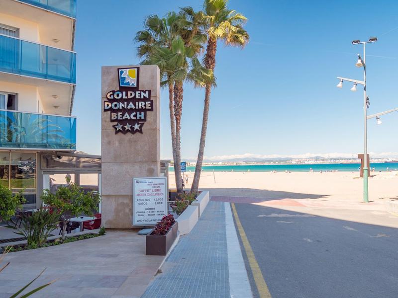 Tablica wejściowa hotelu Golden Donaire Beach z palmami i morzem w tle.