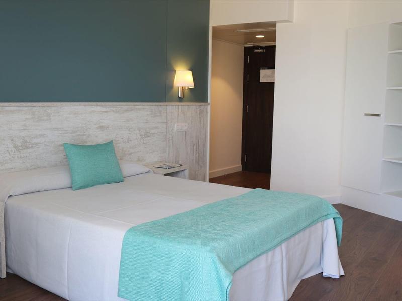 Nowoczesny pokój hotelowy z pojedynczym łóżkiem, turkusowymi akcentami i pośrednim oświetleniem.