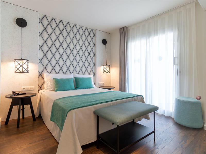 Nowoczesny pokój hotelowy z dużym łóżkiem, turkusową pościelą i przytulnym oświetleniem.