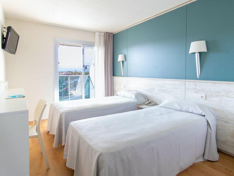 Jasny pokój hotelowy z dwoma łóżkami, niebieską ścianą i małym telewizorem