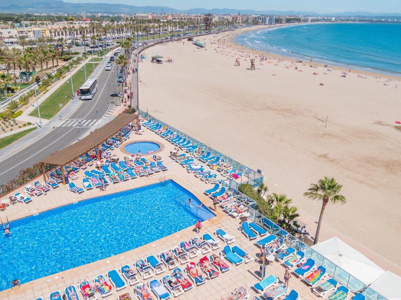 Duży basen z leżakami obok szerokiej piaszczystej plaży i błękitnego morza.