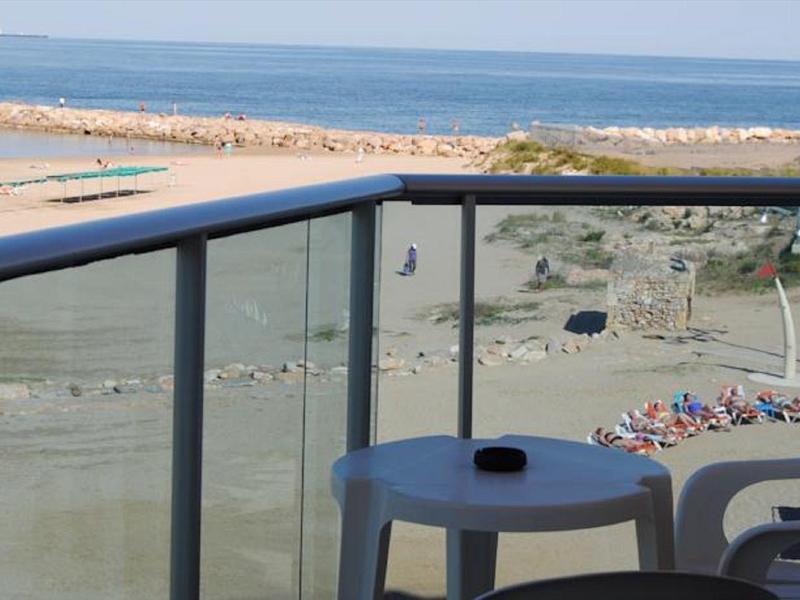 Balkon z stołem i krzesłami z widokiem na plażę i morze przy dobrej pogodzie.