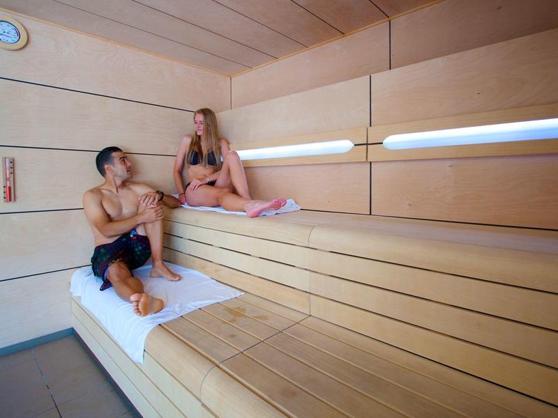 Dwie osoby relaksują się w jasnej, drewnianej saunie z wbudowanym oświetleniem.