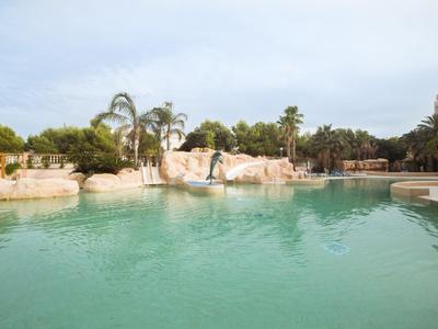 Ein ruhiger Pool mit klarem Wasser, umgeben von Felsen, Palmen und grünen Pflanzen.