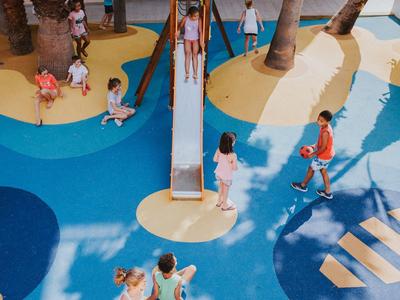 Kinder spielen auf einem bunten Spielplatz mit Rutsche und Palmen.