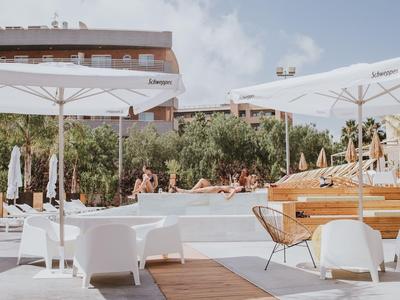 Moderner Außenbereich mit Sonnenliegen und Schirmen neben einem Hotelpool bei klarem Himmel.
