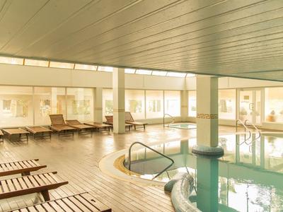 Innenpool mit Liegestühlen und großen Fenstern, warm beleuchtet für Entspannung im Hotel.