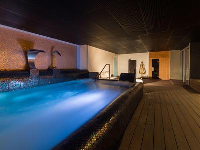 Moderner, gedämpft beleuchteter Innenpool in luxuriösem Wellnessbereich mit Holzfußboden.
