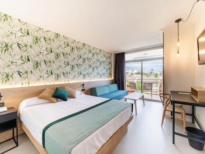Modernes Hotelzimmer mit Doppelbett, Schreibtisch, Sofa und Balkon mit Bergblick.