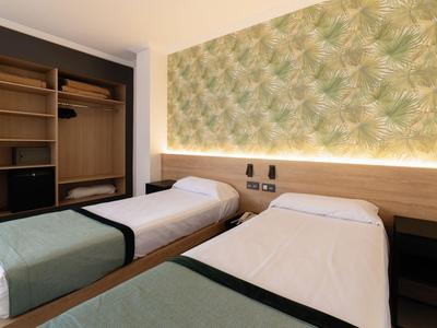 Modernes Hotelzimmer mit zwei Einzelbetten, holzfarbenen Möbeln und grüner Wandgestaltung.