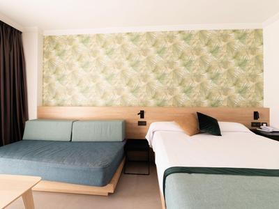 Modernes Hotelzimmer mit Doppelbett, Schlafsofa und grün gemusterter Wandgestaltung.