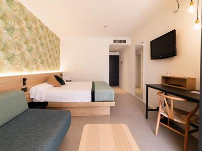 Modernes Hotelzimmer mit Bett, Sofa, Schreibtisch und Fernseher in neutralen Farben.