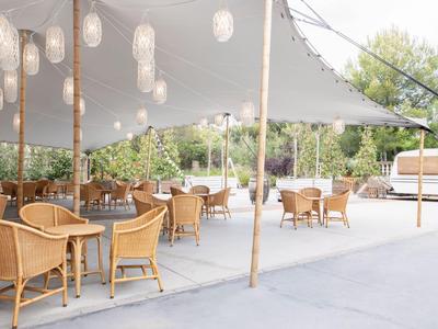 Außerbereich eines Hotels mit Holztischen, Stühlen und Sonnensegeln auf Terrasse.