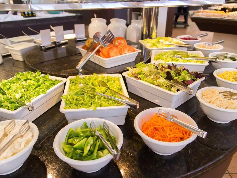 A buffet with various fresh salad ingredients in white bowls on a dark countertop.