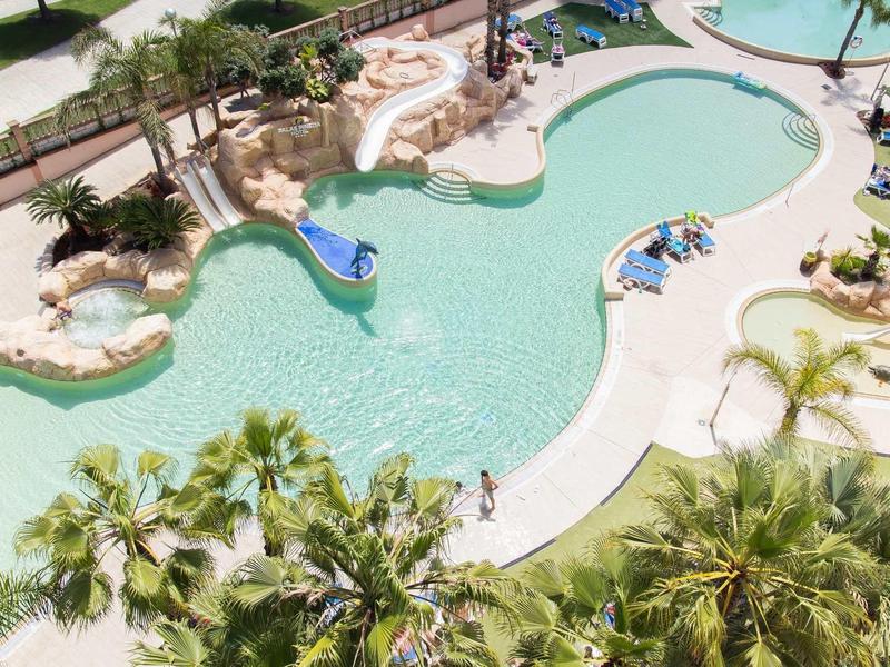 Resort pool with slides, surrounded by palm trees and lounge chairs.