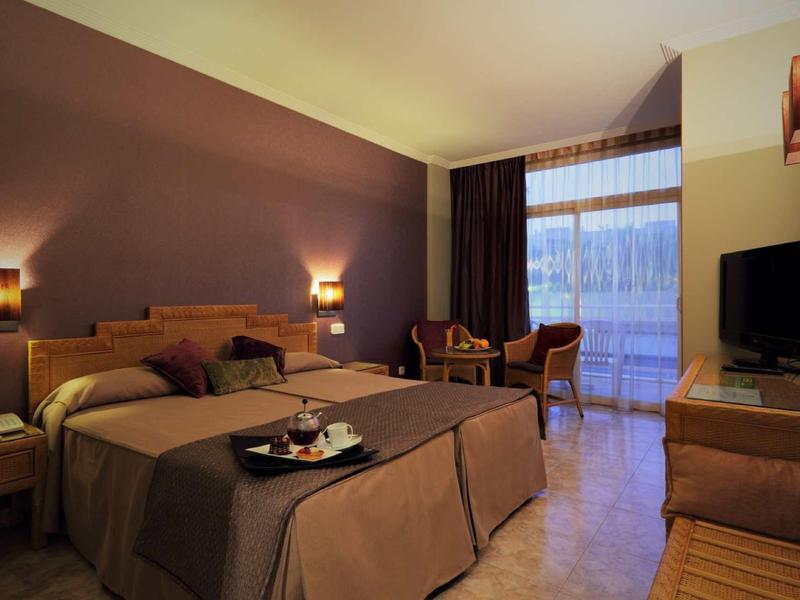 Cozy hotel room with two beds, wooden furniture, and large window with curtains.