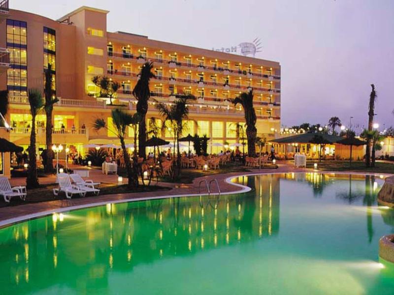 Hotel with illuminated balconies beside a palm-lined pool at dusk