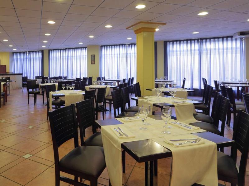 Spacious hotel restaurant with tables set for dining and large windows with curtains.