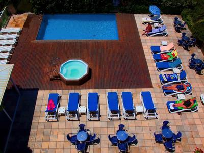 Schwimmbad mit großem blauen Pool, kleinem Rundbecken, Liegestühlen und Tischen mit Stühlen rundherum.