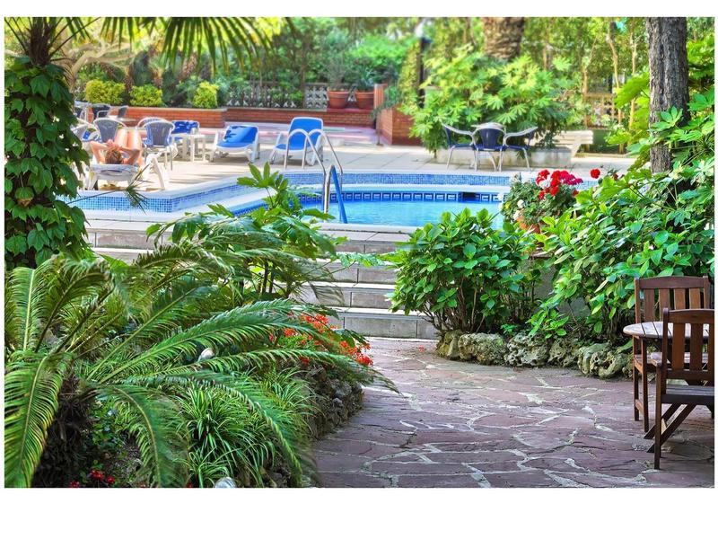 Ein Gartenweg führt zu einem Pool, umgeben von grünen Pflanzen und Sitzgelegenheiten.