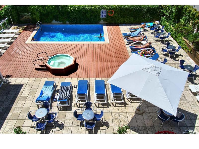 Schwimmbad mit blauer Wasserfläche, hölzernem Deck, Whirlpool, Liegestühlen und Sonnenschirm.