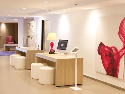 Lounge moderno dell'hotel con banco reception in legno, sgabelli bianchi e opera d'arte rossa.