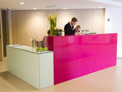 Area di ricezione con una scrivania rosa acceso e due operatori al servizio degli ospiti.