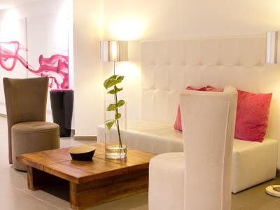 Accogliente salotto dell'hotel con illuminazione soffusa, divani beige, tavolo in legno e cuscini rosa decorativi.